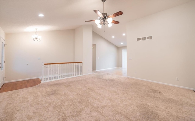 carpeted empty room with high vaulted ceiling and ceiling fan with notable chandelier