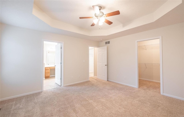 unfurnished bedroom featuring a walk in closet, light colored carpet, a raised ceiling, ceiling fan, and a closet