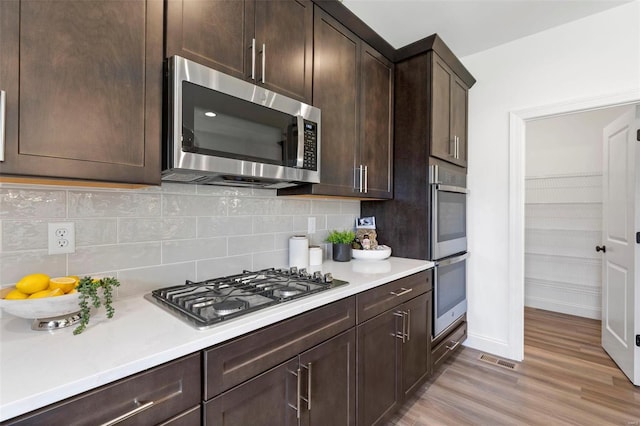 kitchen featuring appliances with stainless steel finishes, light wood-type flooring, tasteful backsplash, and dark brown cabinets