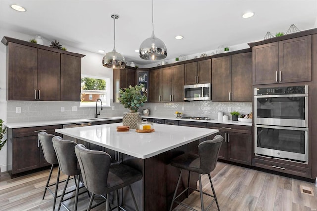 kitchen featuring dark brown cabinets, stainless steel appliances, light hardwood / wood-style flooring, and hanging light fixtures