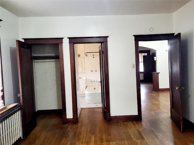 unfurnished bedroom with a closet, connected bathroom, dark hardwood / wood-style floors, and radiator