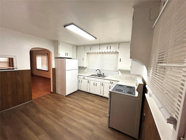 kitchen with wood walls, stove, white cabinets, white refrigerator, and sink