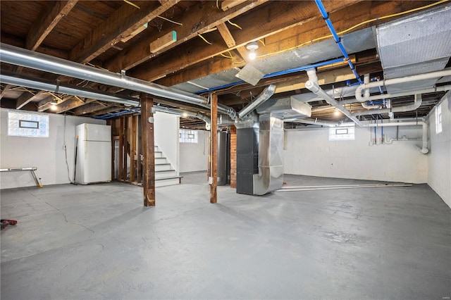 basement featuring plenty of natural light, white refrigerator, and heating unit