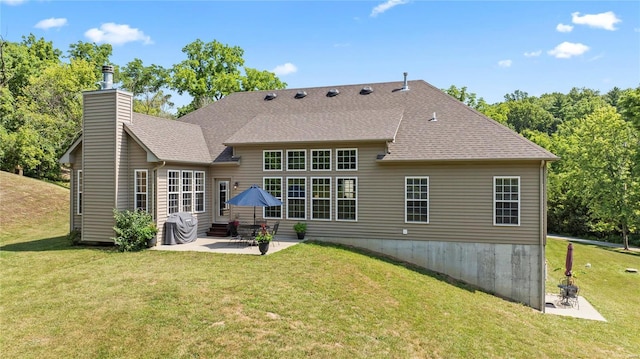 rear view of house with a yard, roof with shingles, a patio, and a chimney