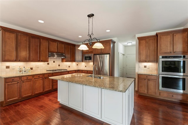 kitchen with under cabinet range hood, stainless steel appliances, dark wood-style flooring, light stone countertops, and tasteful backsplash