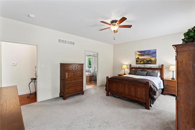 bedroom with ceiling fan, light carpet, visible vents, baseboards, and ensuite bath