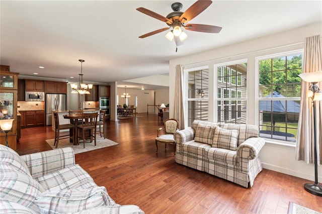 living area with ceiling fan with notable chandelier, dark wood finished floors, and baseboards