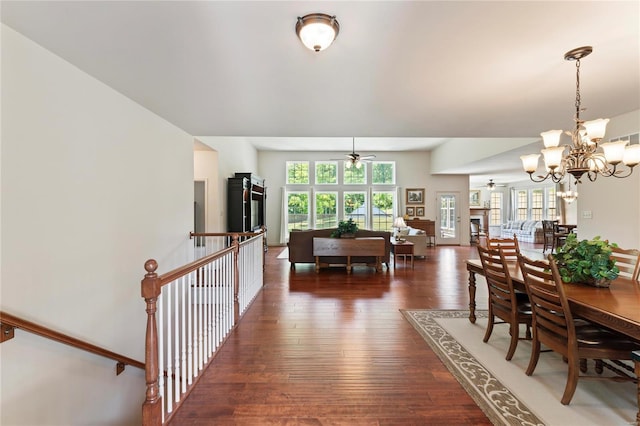 dining space with ceiling fan with notable chandelier, dark wood-style flooring, a fireplace, and a wealth of natural light