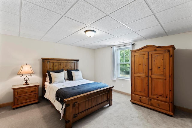 bedroom with a paneled ceiling, light carpet, and baseboards