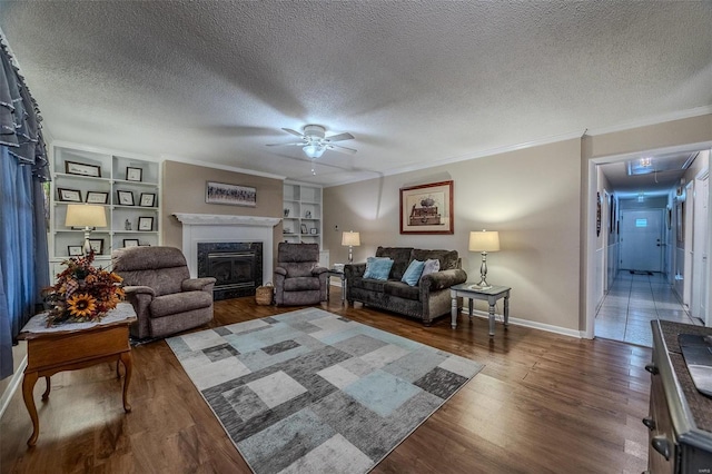 living room with a high end fireplace, ceiling fan, built in features, a textured ceiling, and ornamental molding