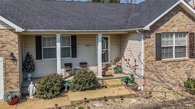 view of exterior entry featuring brick siding, a porch, and roof with shingles