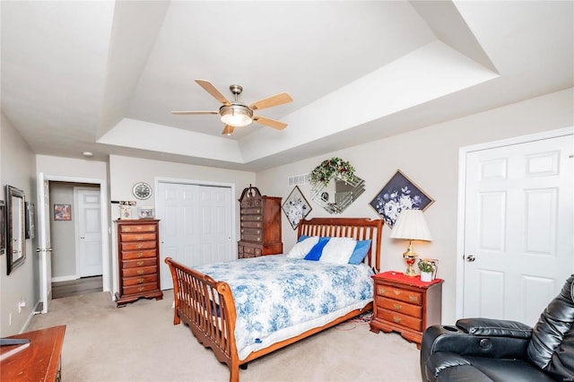 bedroom with visible vents, a closet, a raised ceiling, light colored carpet, and ceiling fan