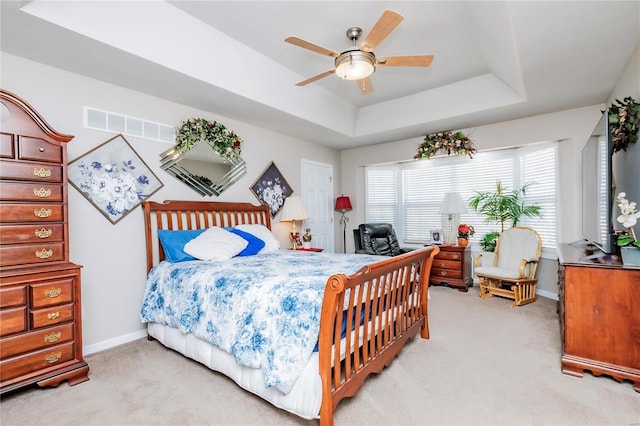 bedroom featuring a ceiling fan, visible vents, baseboards, a tray ceiling, and light colored carpet