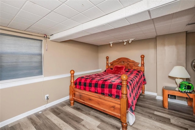 bedroom featuring rail lighting, wood finished floors, baseboards, and a drop ceiling