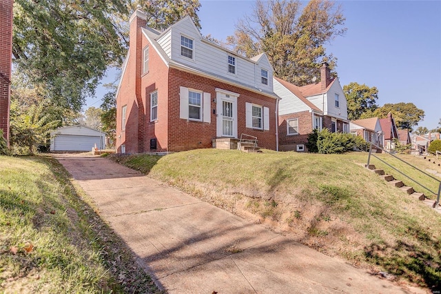 view of front of home with an outbuilding, a garage, brick siding, a chimney, and a front yard