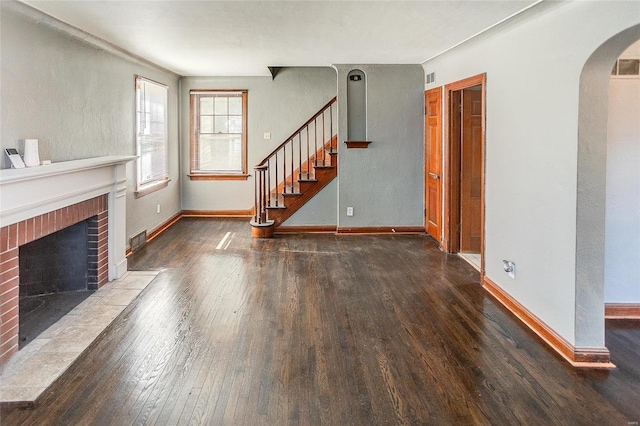 unfurnished living room with arched walkways, baseboards, hardwood / wood-style floors, stairs, and a fireplace