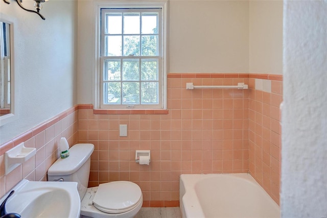 bathroom featuring tile walls, wainscoting, toilet, a bath, and a sink