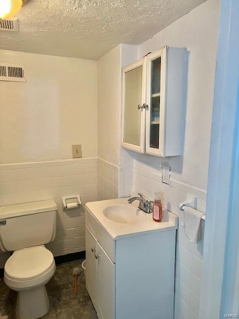 bathroom with a textured ceiling, vanity, tile walls, and toilet