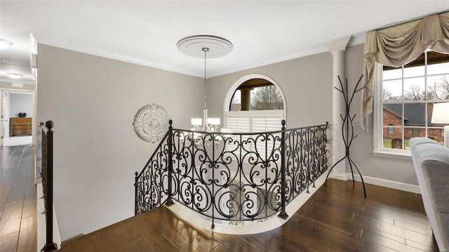 hall featuring dark hardwood / wood-style floors, decorative columns, ornamental molding, and a notable chandelier