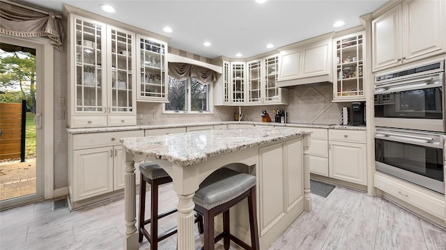 kitchen with decorative backsplash, a kitchen bar, stainless steel double oven, and a healthy amount of sunlight