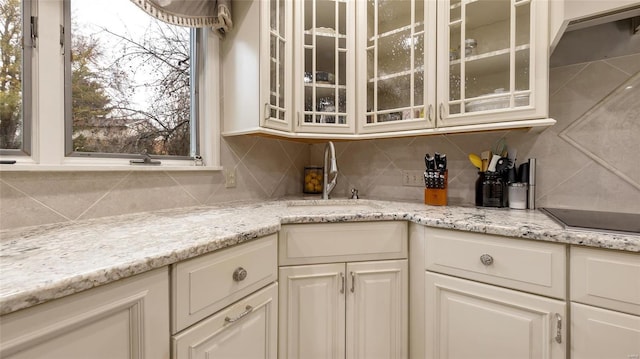 bar with light stone counters, black electric cooktop, sink, and tasteful backsplash