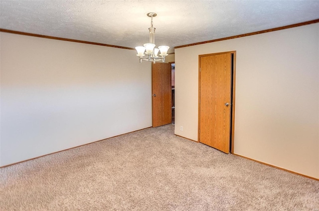 spare room featuring a textured ceiling, ornamental molding, light carpet, and a chandelier