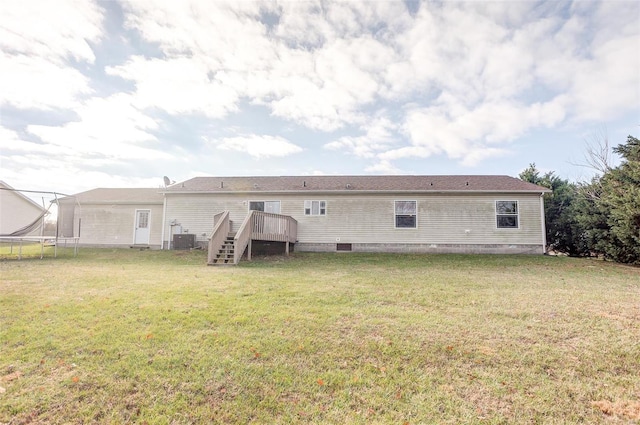 rear view of house with a wooden deck, a yard, central AC unit, and a trampoline