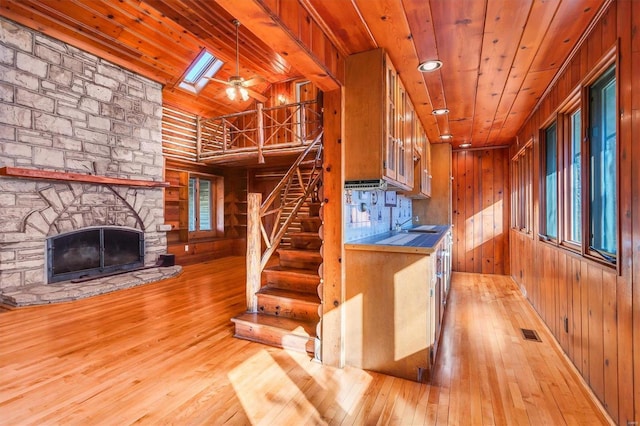 kitchen with a skylight, wood ceiling, light hardwood / wood-style flooring, a stone fireplace, and wood walls