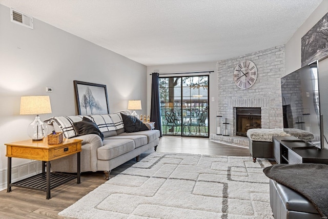 living room with a textured ceiling, hardwood / wood-style flooring, and a brick fireplace