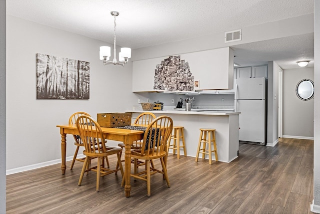 dining room with sink, dark wood-type flooring, a textured ceiling, and a notable chandelier