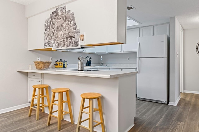 kitchen with white cabinetry, sink, dark wood-type flooring, white refrigerator, and a breakfast bar area