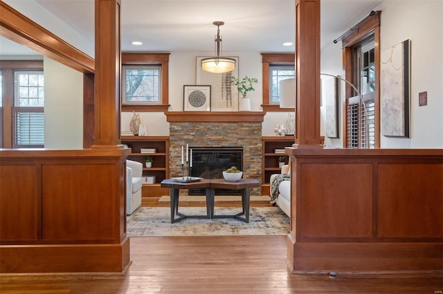 sitting room featuring light wood-type flooring, decorative columns, and a stone fireplace