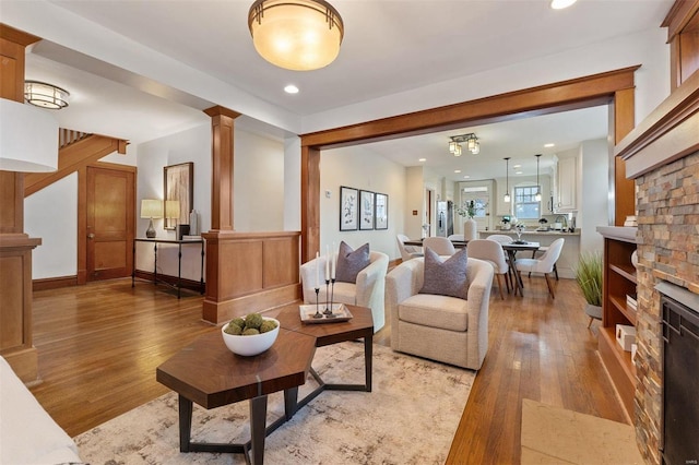 living room with decorative columns, a stone fireplace, and light hardwood / wood-style floors