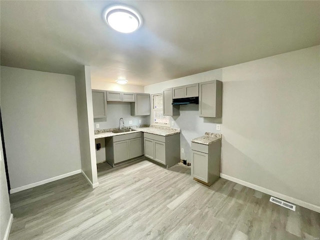 kitchen with gray cabinetry, sink, and light hardwood / wood-style flooring