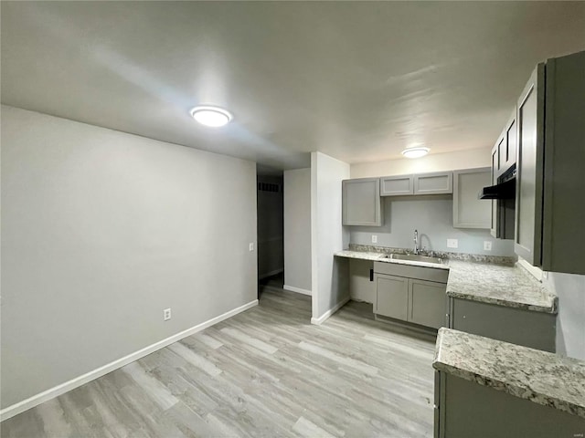 kitchen featuring gray cabinets, light stone countertops, sink, and light hardwood / wood-style flooring