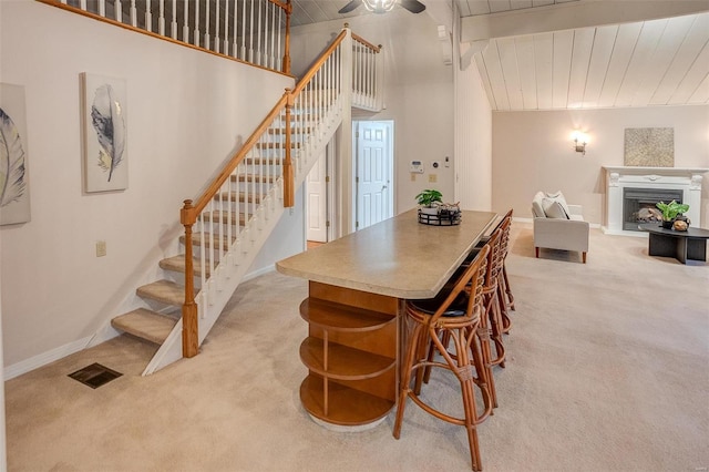 dining space with light carpet, a towering ceiling, ceiling fan, and wooden ceiling