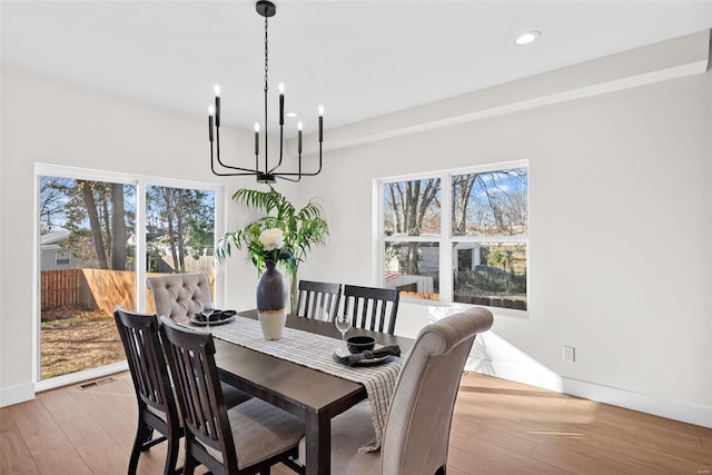 dining area with light wood-type flooring, a wealth of natural light, and a notable chandelier