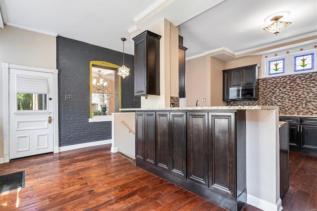 kitchen with dark brown cabinetry, a notable chandelier, brick wall, and pendant lighting