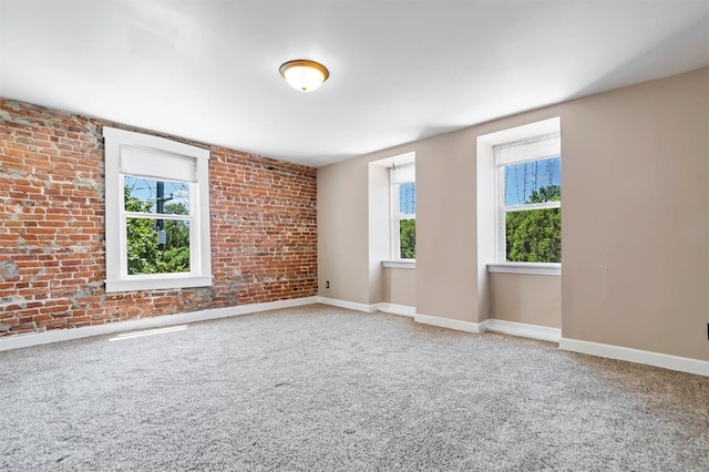 carpeted spare room featuring a healthy amount of sunlight and brick wall