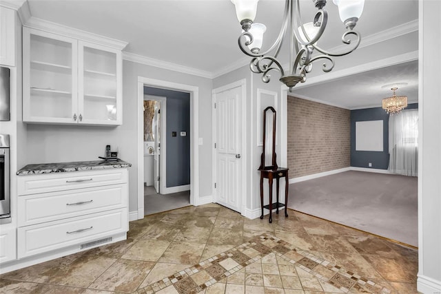 unfurnished dining area featuring carpet flooring, crown molding, brick wall, and a chandelier