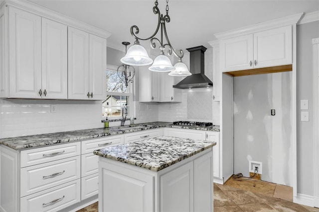 kitchen featuring sink, wall chimney range hood, decorative light fixtures, white cabinets, and a center island