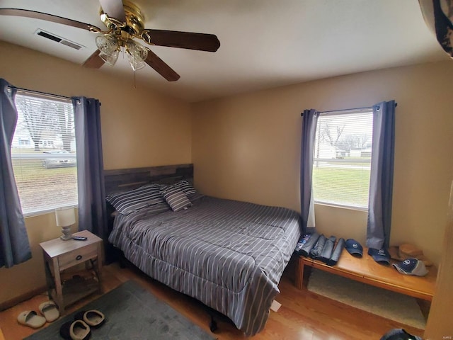 bedroom with a ceiling fan, wood finished floors, visible vents, and multiple windows