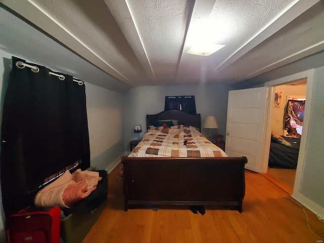 bedroom with light wood-type flooring, lofted ceiling, and a textured ceiling