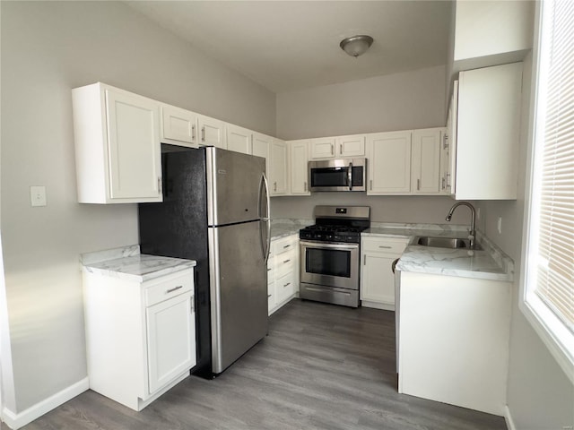 kitchen with light stone counters, stainless steel appliances, sink, hardwood / wood-style floors, and white cabinetry