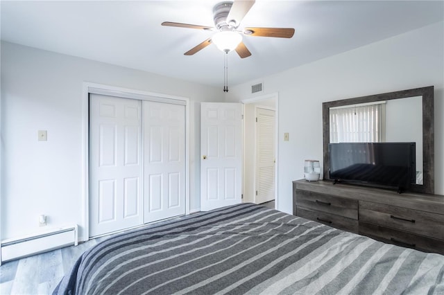 bedroom featuring hardwood / wood-style floors, ceiling fan, baseboard heating, and a closet