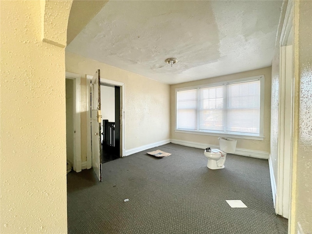 spare room featuring dark carpet and a textured ceiling