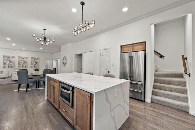 kitchen featuring appliances with stainless steel finishes, light stone counters, an inviting chandelier, a center island, and hanging light fixtures