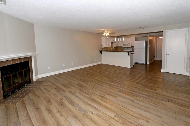 unfurnished living room with a textured ceiling, ceiling fan, dark hardwood / wood-style flooring, and a fireplace