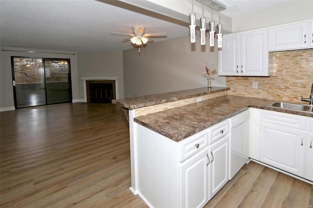 kitchen featuring kitchen peninsula, white dishwasher, sink, decorative light fixtures, and white cabinetry