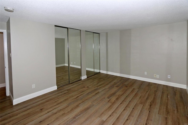 unfurnished bedroom with a textured ceiling, dark hardwood / wood-style floors, and multiple closets